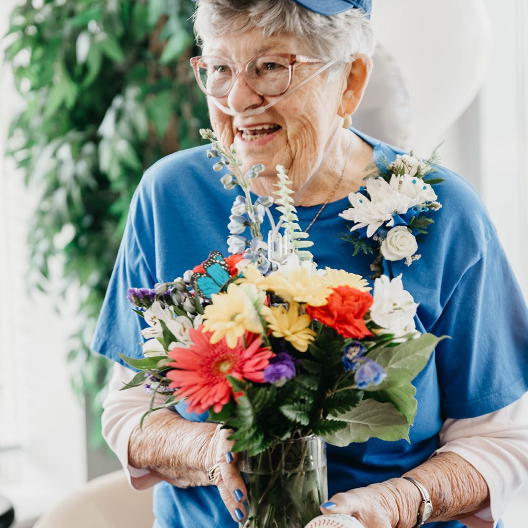 Shirley, holds a flower bouquet and a ball with Blue Jays mark, is smiling. / Shirley, qui tient un bouquet de fleurs et un ballon portant la marque des Blue Jays, sourit.